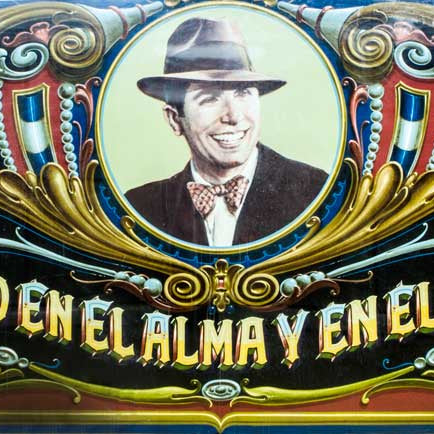 A picture of the tango musician Carlos Gardel, decorated with fileteado porteño. Below the photograph can be read, in Spanish, "Eterno en el alma y en el tiempo"
